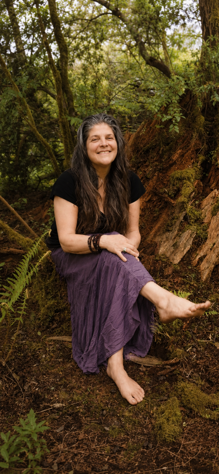 Joy Bird Wilson, Licensed Massage Therapist, seated in a mossy Pacific Northwest forest